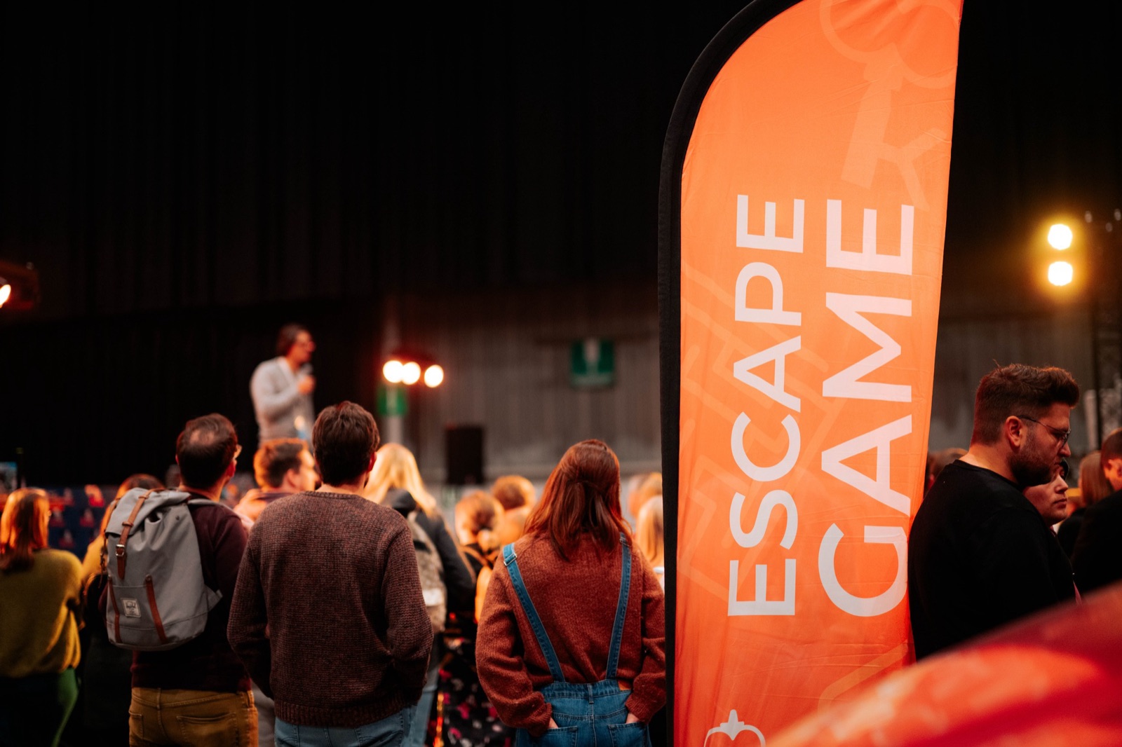 Bezoekers op een evenement, naast een vlag met Escape Game